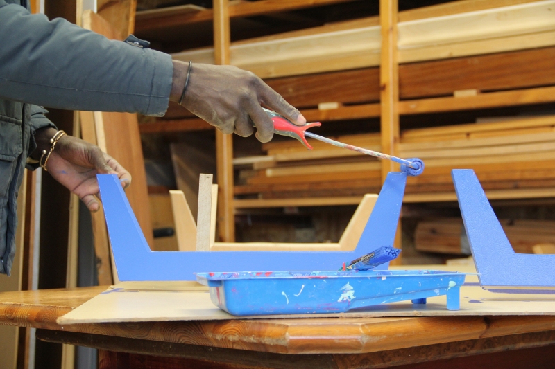 Un compagnon Emmaüs peint un meuble